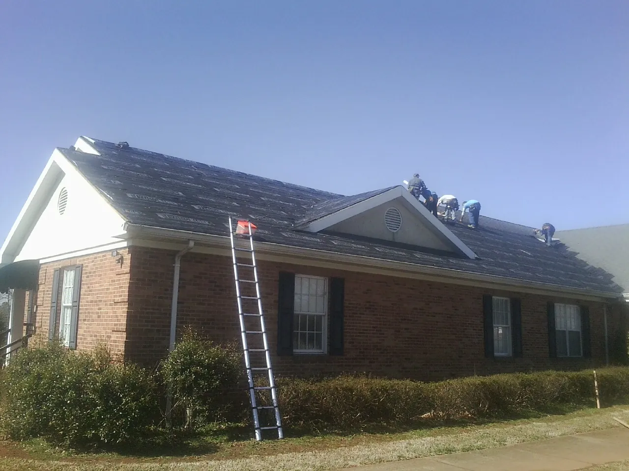 Crew tearing shingles off a brick ranch roof with a ladder set — Metal Roof Repair work by our crew in Harrisville