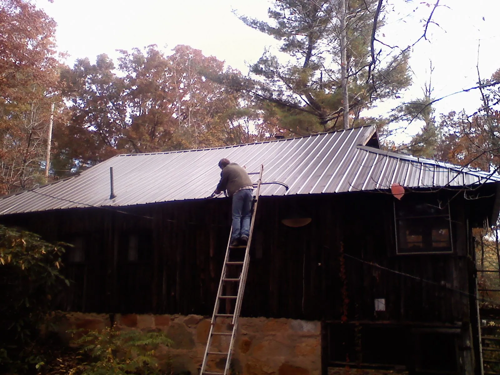 Roofer on a ladder working along the edge of a cabin metal roof in Harrisville